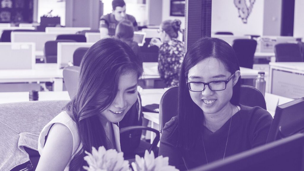 Two workmates smiling at the computer