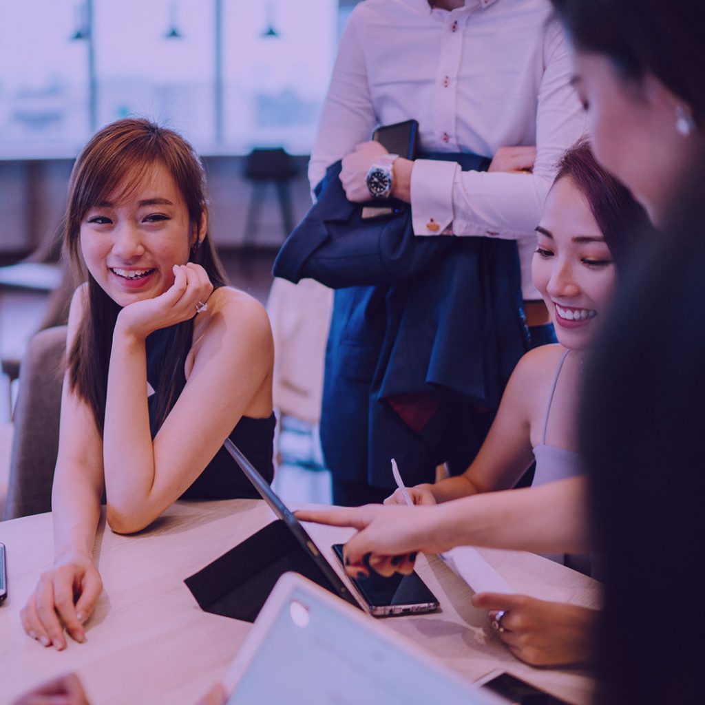 Table surrounded by salespeople smiling and using gadgets.